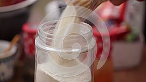 Pouring wheat flour from paper bag to jar - closeup