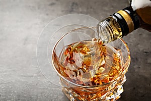 Pouring whiskey from bottle into glass with ice cubes