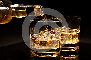 pouring whiskey into a glass from bottle with ice cubes on black