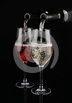 Pouring of white and red wine from bottles into glasses on dark background