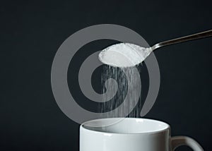 Pouring white sugar from spoon to white coffee cup, mug