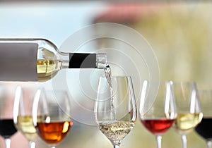 Pouring white wine from bottle into glass on blurred background, closeup
