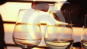 Pouring white wine in four glasses at amazing sunset by the sea in beach cafe before partying in slow motion. 3840x2160