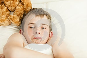 Pouting boy in bed covered with blanket