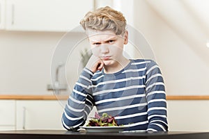 Pouting boy sitting in front of salad greens