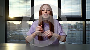 POV of cheerful young woman blogger greeting followers during video call sitting at desk on background of window.