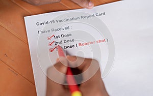POV close up shot of hands checking Covid-19 vaccine report card and ticking 3rd or booster dose after vaccination photo