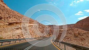 POV Driving a car going down on asphalt Eilat road with rocky mountains. Sunny sky with white clouds