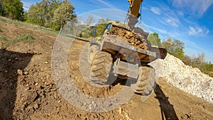 POV: Excavator arm scoops up a bucket full of soil and dumps it on the trailer.