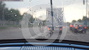 POV from the front seat to windshield of old retro car during bad weather. Wipers removing raindrops from the window of