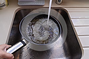 Frying pan with non-stick surface and hot oil under water tap flow in sink photo