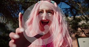 POV: girl with pink hair posing, grimacing and scaring in front of the camera. Halloween day, pink clothes and pink hair