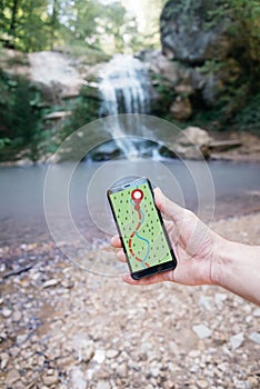 POV of hand with smartphone GPS app in nature near waterfall.