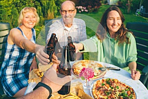 POV image of people toasting with beer bottles at multi generation family backyard party