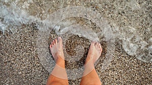 POV of male feet standing on the sea beach and enjoying rolling calm waves with clear water. Holiday, summer vacation