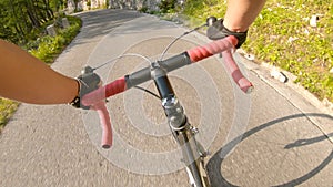 POV: Male riding a road bike up a steep asphalt road running through the forest.