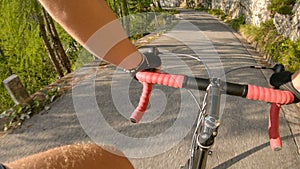 POV: Pedalling a road bicycle up a steep asphalt road in the sunny mountains.