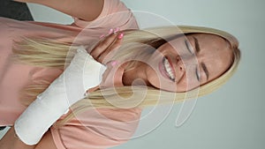 POV portrait of cheerful blonde young woman with broken arm wrapped in white plaster bandage talking via video chat