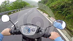 POV: Riding a motorcycle along empty road leading through the tropical forest.