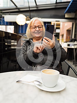 pov senior happy woman enjoying with the cell phone with the coffees already finished