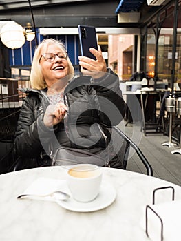 pov senior woman laughing watching selfie with cell phone with already finished coffees