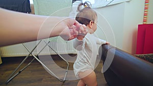 pov shot of a baby first steps of baby learning to walk at home helped by the mother.