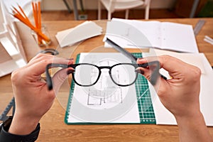 POV Shot Of Female Architect Holding Glasses Working In Office On Plans For New Building