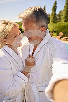 POV Shot Of Senior Couple In Robes Outdoors By Swimming Pool On Spa Day