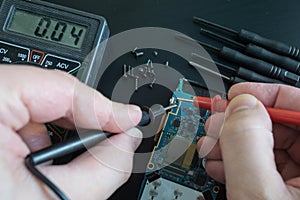 Pov shot of technician hands measure voltage, amperage on broken smartphone by multimeter with probes
