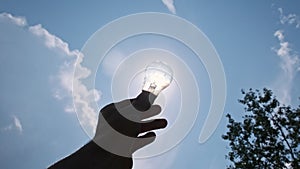 POV Silhouette of Male Hand Holds Light bulb Against Bright Sun and Blue Sky