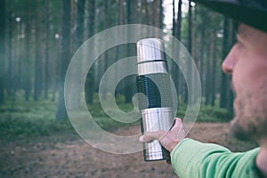POV tourist man hand with stainless thermos in forest. Hiker on trail in forest, local travel, active outdoor lifestyle