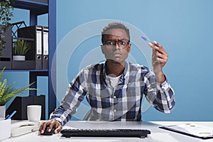 POV of unsure suspicious office administrator having pen in hand looking mistrustful at computer monitor.