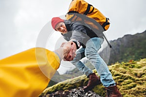 POV view on brave tourist helping his active friend holding to hand climbing to rock photo