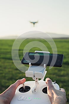 POV view - Man control the drone by remote control over the meadow on sunset. Man operating the drone and flying over the field