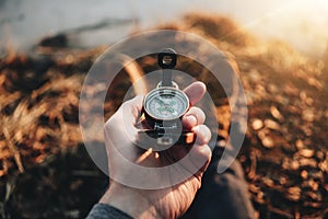 POV view of traveler hold compass in hand and legs in hiking boot. Blurred background