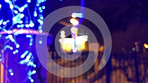 POV walking along hanging garland of blue neon Christmas lights at night city. Christmas ornaments outdoors. Magical