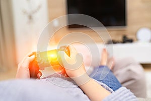 POV Woman lying on the coach in front of TV and holding in hands wireless game controller. Game addiction concept.