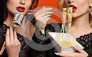 Poverty and wealth concept. Rich and poor girls friends hold stack of money dollars cash  Chinese chopsticks eating cheap noodles