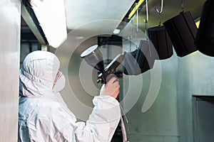 Powder coating of metal parts. A man in a protective suit sprays powder paint from a gun on metal products