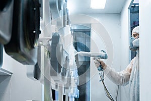 Powder coating of metal parts. Man in a protective suit sprays white powder paint from a gun on metal products