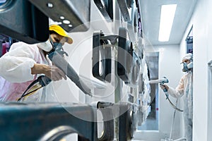 Powder coating of metal parts. Man and woman in protective suit sprays white powder paint from gun on metal products