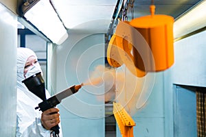 Powder coating of metal parts. A woman in a protective suit sprays powder paint from a gun on metal products