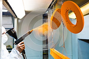 Powder coating of metal parts. A woman in a protective suit sprays powder paint from a gun on metal products photo