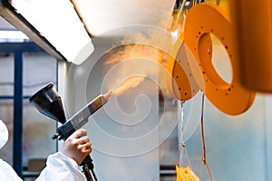 Powder coating of metal parts. A woman in a protective suit sprays powder paint from a gun on metal products