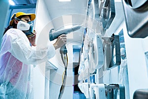 Powder coating of metal parts. A woman in a protective suit sprays white powder paint from a gun on metal products