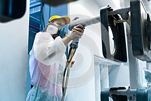 Powder coating of metal parts. A woman in a protective suit sprays white powder paint from a gun on metal products