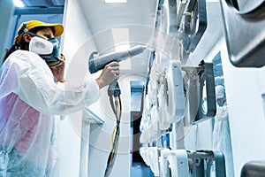 Powder coating of metal parts. A woman in a protective suit sprays white powder paint from a gun on metal products