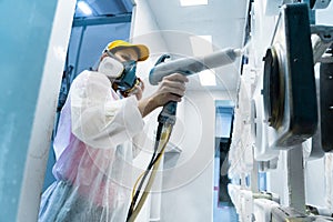 Powder coating of metal parts. A woman in a protective suit sprays white powder paint from a gun on metal products