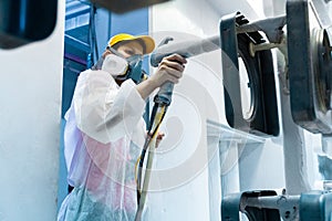 Powder coating of metal parts. A woman in a protective suit sprays white powder paint from a gun on metal products