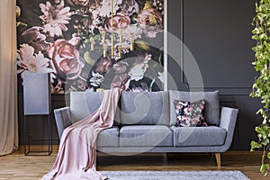 Powder pink blanket thrown on grey couch in real photo of dark s